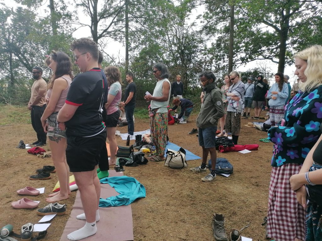 A group of people meditate in a wood In Vegan Camp Out.