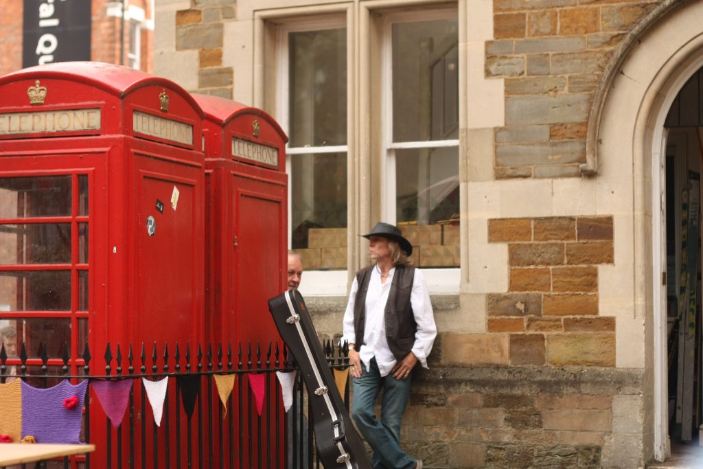 A musician stands next to red telephone box