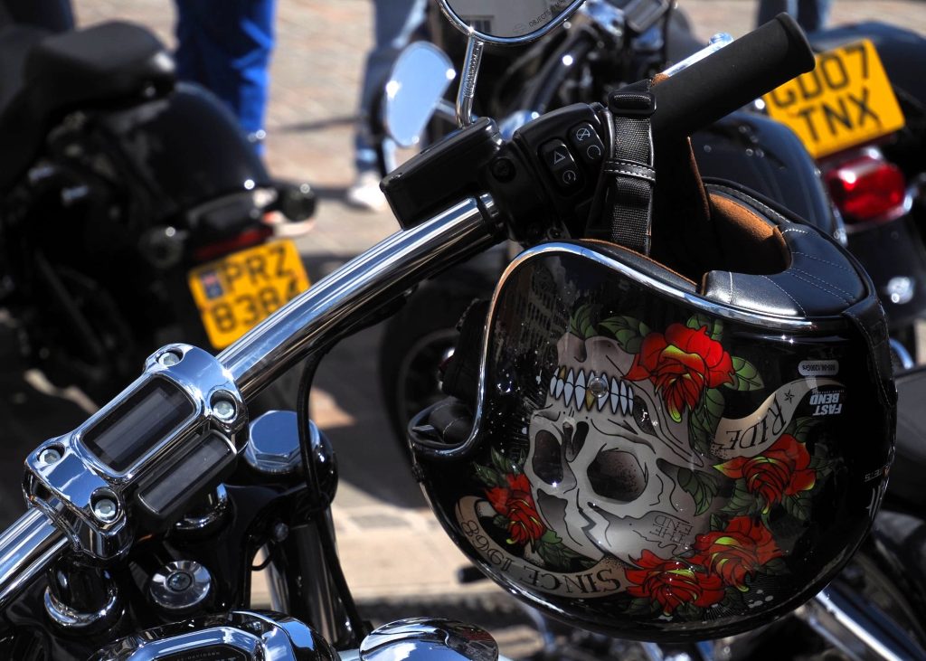A helmet with skull and rose hangs on motorcycle handlebars